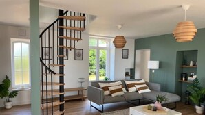 Un salon moderne avec un escalier en colimaçon, un canapé gris, une table basse blanche et un mur d’accent vert.