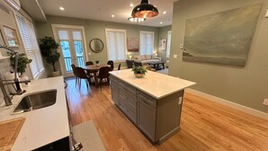 Een moderne keuken met een centraal eiland, houten vloeren en een eethoek met stoelen en een tafel.