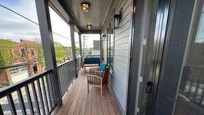 Een overdekt balkon met houten vloer, twee houten stoelen en een tafel.