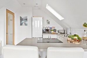 A modern kitchen with a dining area, featuring a wooden table, white chairs, and a built-in oven.