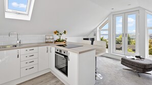 Eine moderne Küche mit weißen Schränken, einem Backofen, einer Spüle und einem Fenster mit Blick auf eine reizvolle Landschaft.