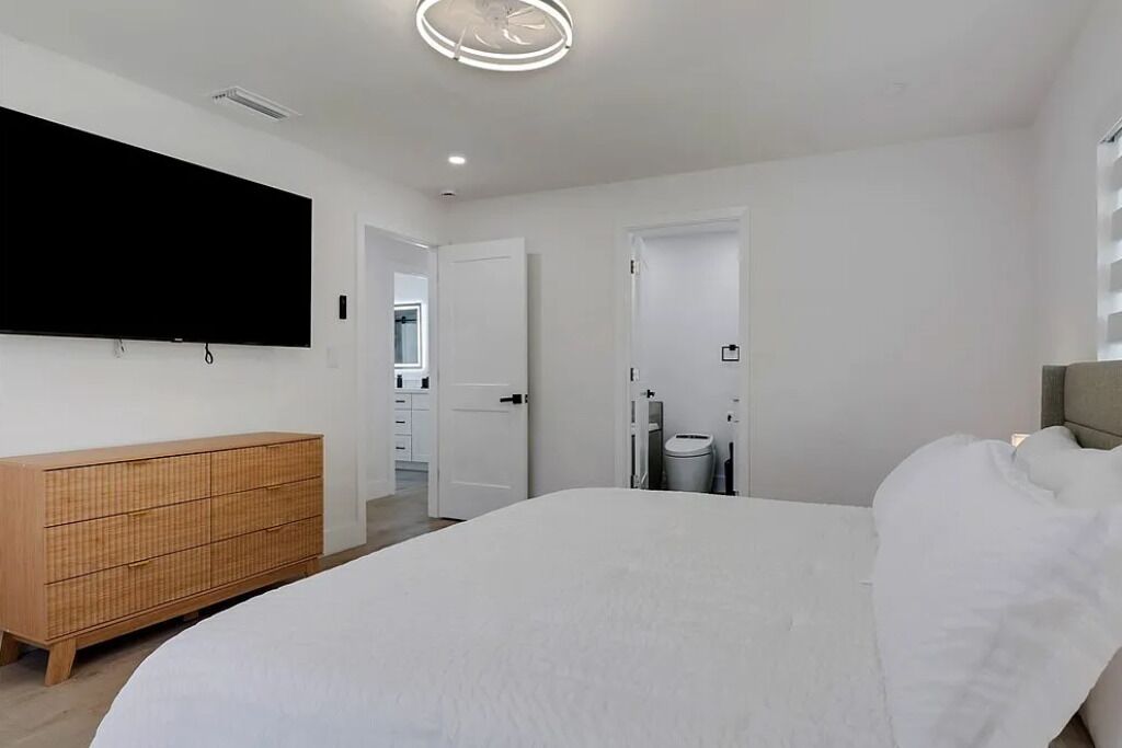 Un dormitorio moderno con una cama grande, un aparador de madera, un televisor de pantalla plana en la pared y un ventilador de techo.