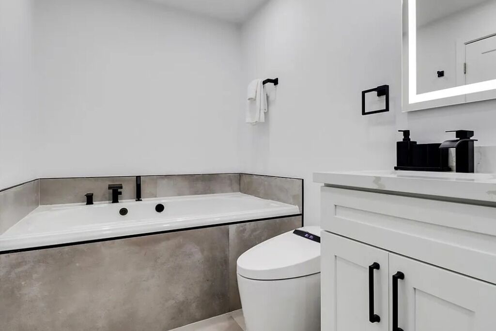 A modern bathroom with a large white bathtub, a toilet, and a vanity with a mirror.