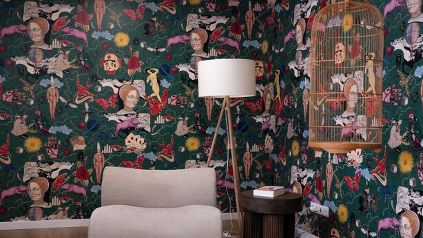 Une pièce avec un papier peint à motifs verts, un canapé beige, un lampadaire et une cage à oiseaux.