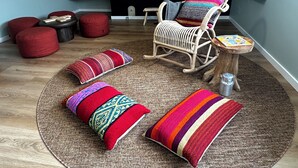 A cozy living room with a wicker rocking chair, red poufs, a woven rug, and a small wooden table. - Storyteller's Retreat. Design and comfort in the historic center of Ponta Delgada! (Ponta Delgada)