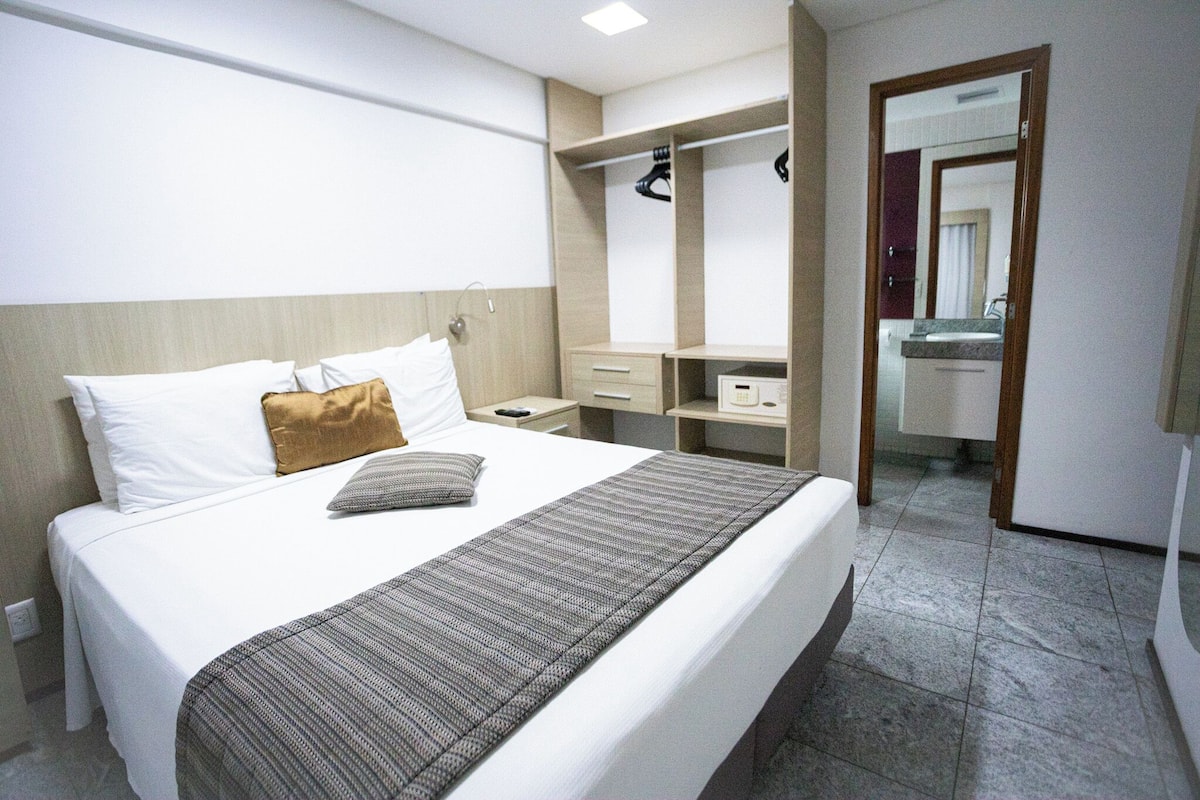 A hotel room with a bed, a bedside table, a wardrobe, and a mirror.