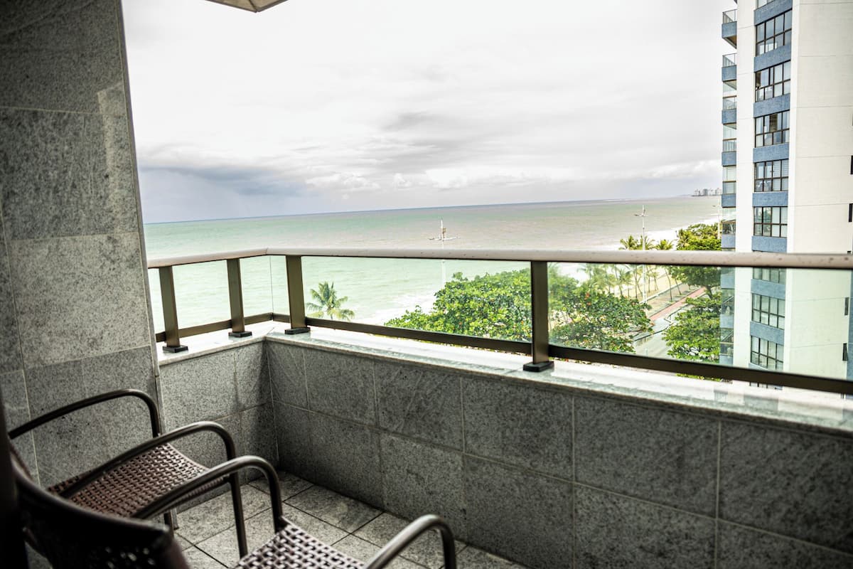 A balcony with a view of the ocean and a building in the background.