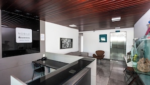 A modern reception area with a glass counter, a phone, and a seating area with chairs. There is a framed picture on the wall and a glass display case with items.