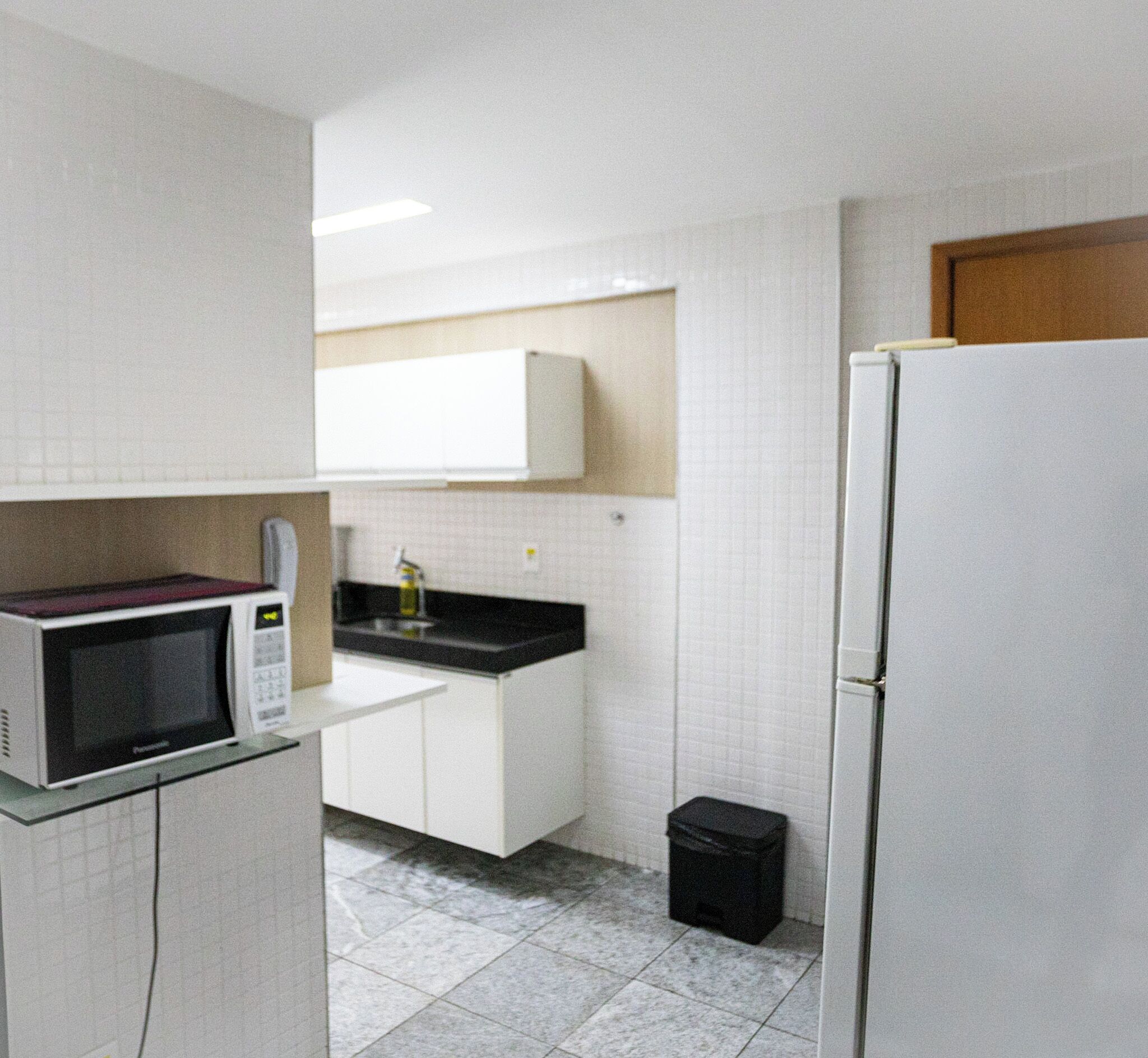 A compact kitchen with white cabinets, a microwave, a black countertop, and a refrigerator.