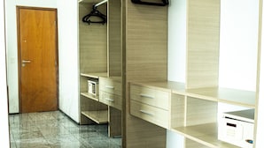 A modern room with a wooden door, a mirror, a wardrobe with hanging space, and a small desk with drawers.