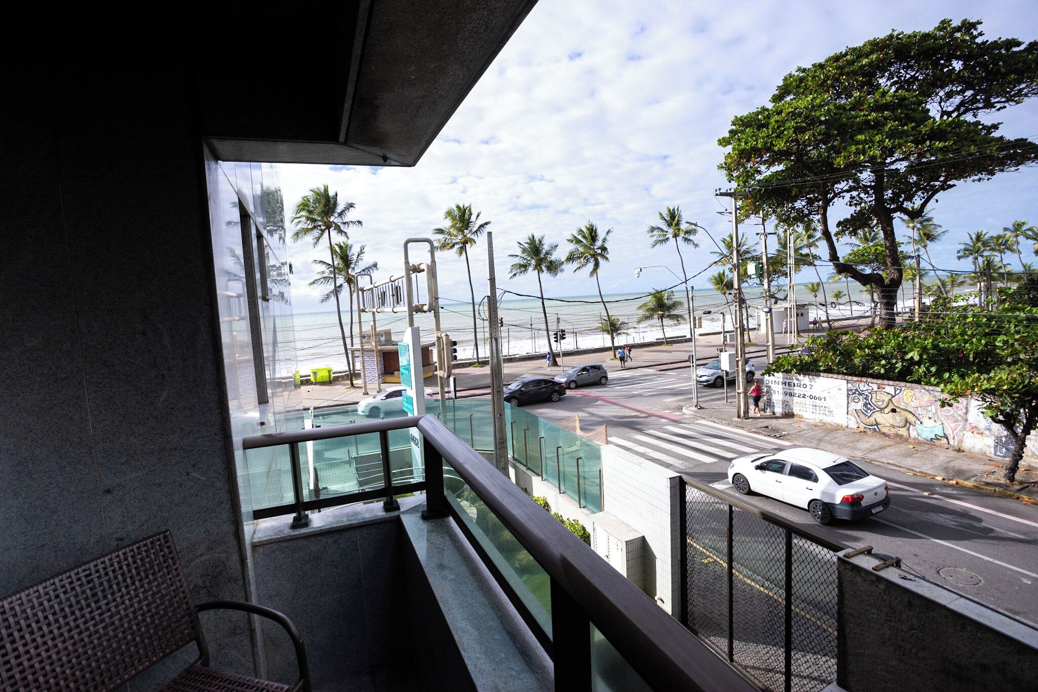 Uma varanda com vista para uma rua, palmeiras e o oceano.