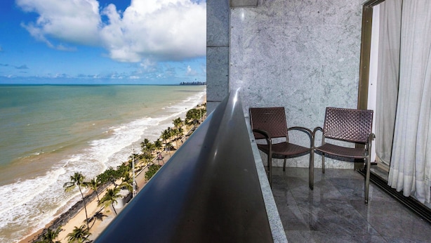 A balcony with a view of the beach and ocean, two wicker chairs, and a marble wall.