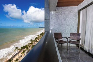 A balcony with a view of the beach and ocean, two wicker chairs, and a marble wall. - FLAT NOBILE RESIDENCES MARIA FRAZÃO (Recife)