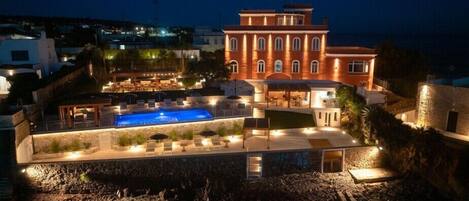 A large building with a swimming pool, outdoor seating, and a stone wall.