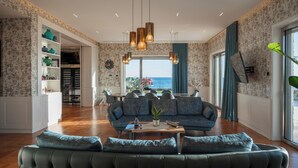 A spacious living room with a large sofa, a coffee table, and a view of the sea through large windows. - Villa Giada Luxury Boutique (Civitavecchia)