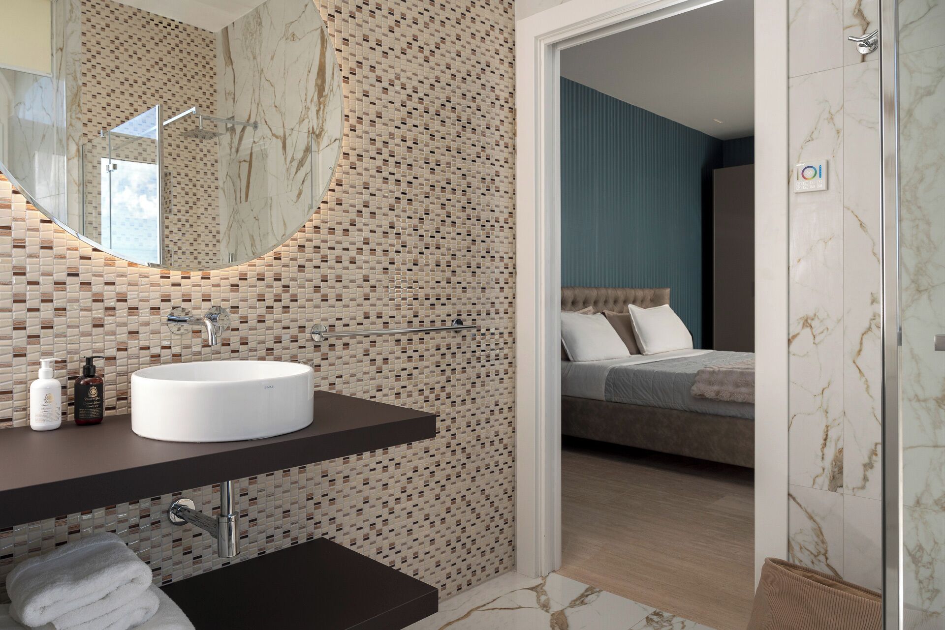 A modern bathroom with a round sink, a glass shower enclosure, and a mosaic tile backsplash.