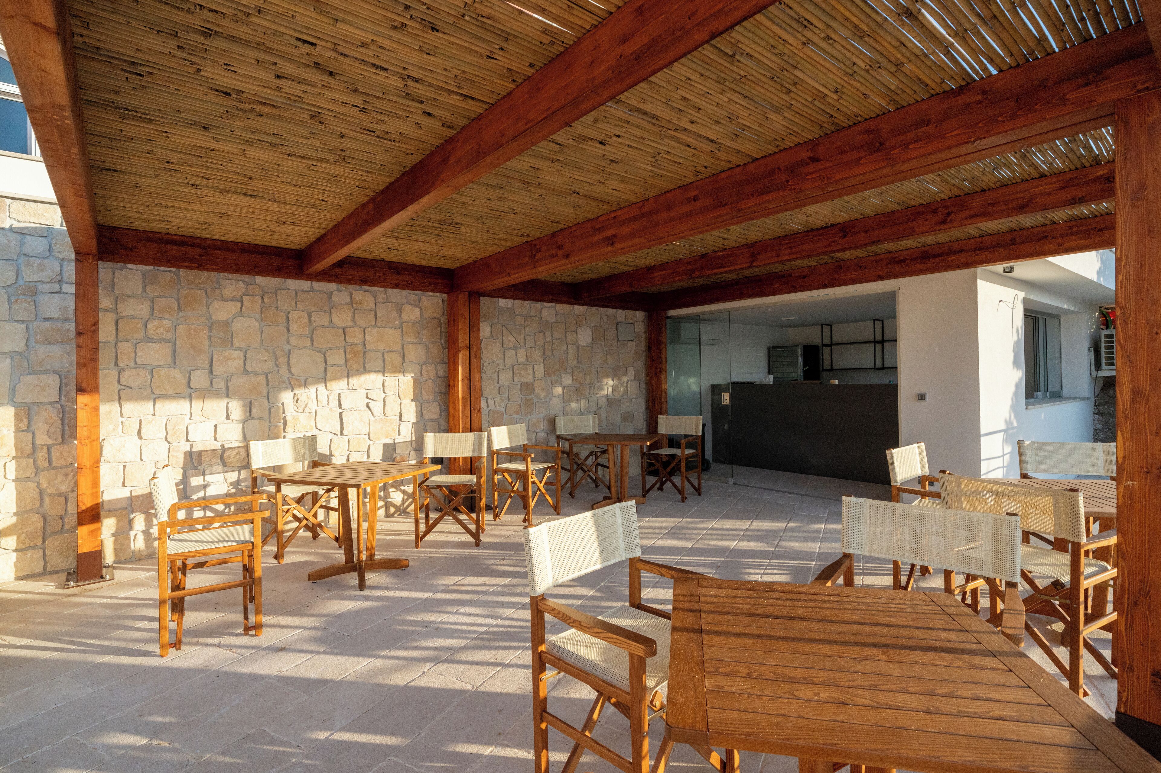 Un espace extérieur aménagé en terrasse, avec des tables et des chaises en bois, des murs en pierre et une vue sur l’intérieur.