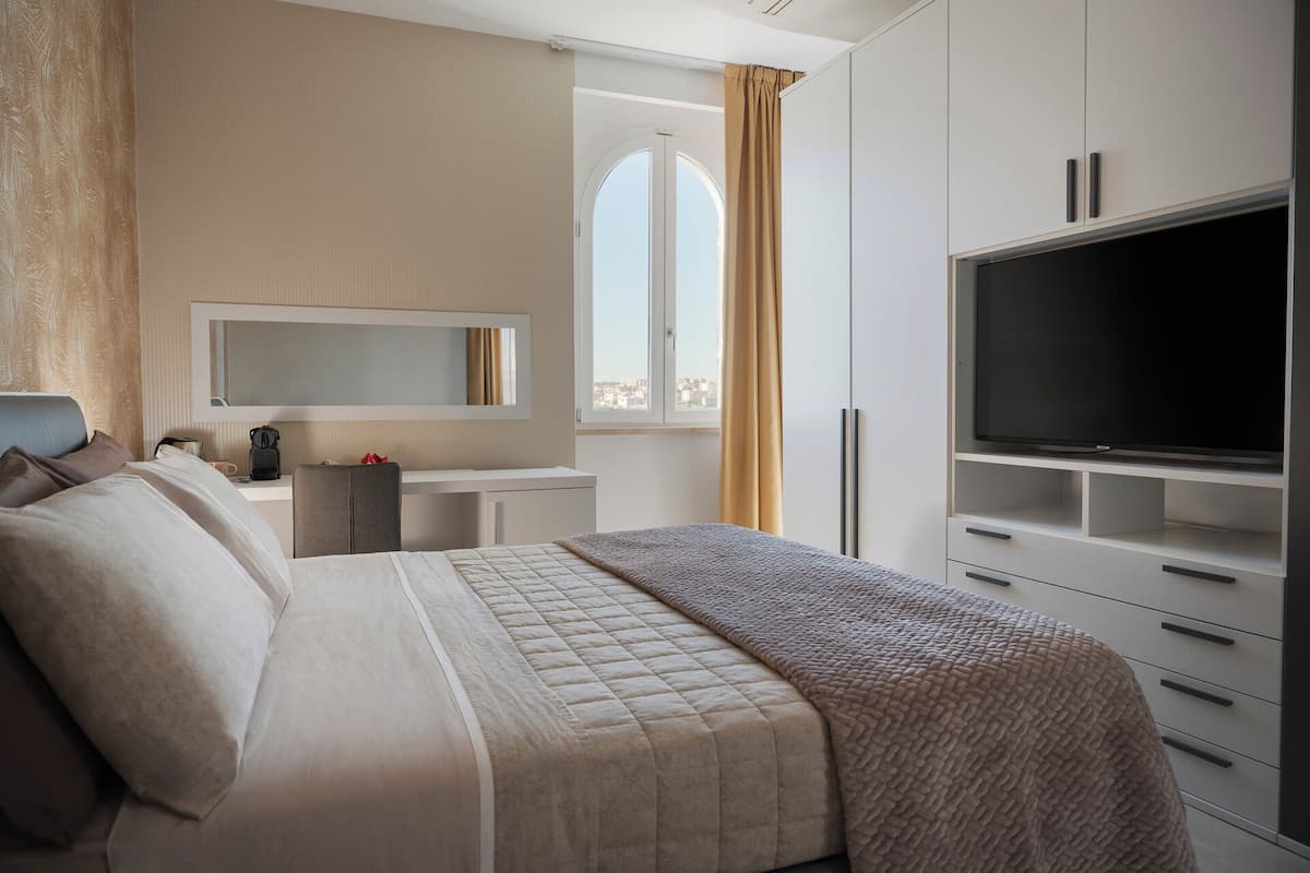 Una habitación de hotel con cama, televisión, escritorio y ventana con cortinas.