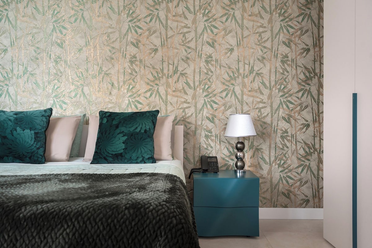 Un dormitorio con cama, almohadas, una lámpara de noche y una mesita de noche.