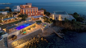 A coastal hotel with a swimming pool, outdoor seating, and a view of the sea.