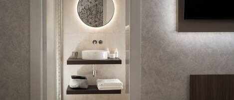 Un baño moderno con un espejo redondo, un lavabo blanco y dos estantes con artículos de aseo.