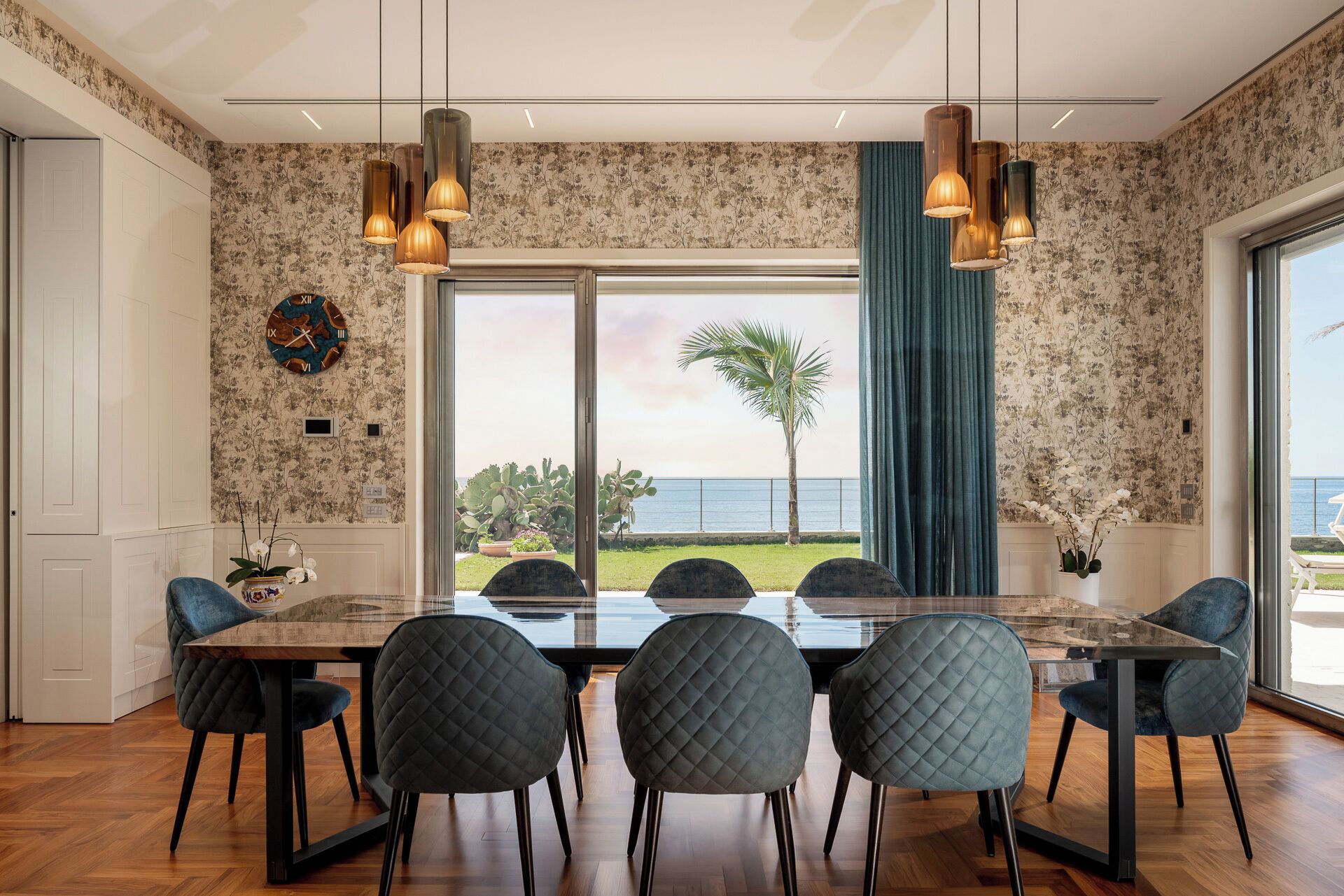 Un coin repas avec une grande table et six chaises, une vue sur l’océan et une plante tropicale à l’extérieur.