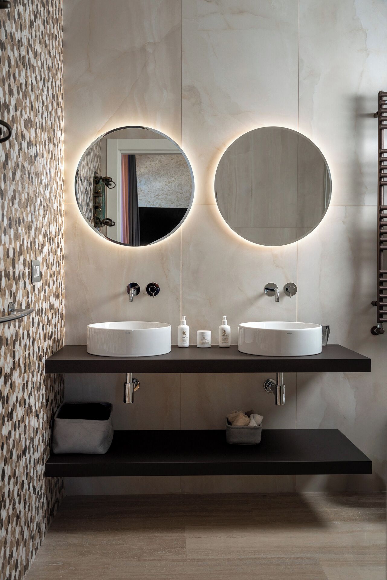 Une salle de bain moderne avec deux miroirs ronds, un lavabo double et un porte-serviettes.