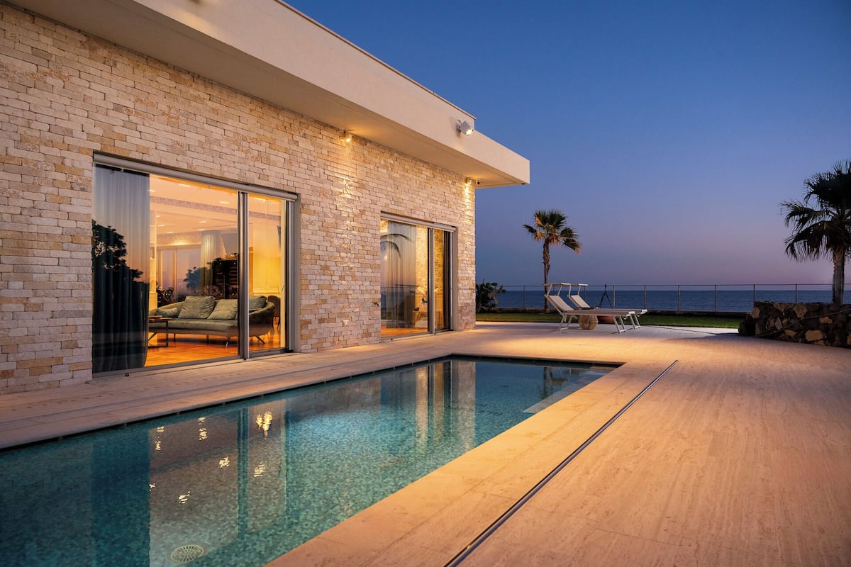 Una casa moderna con piscina, un patio con sillones de descanso y vistas al mar.