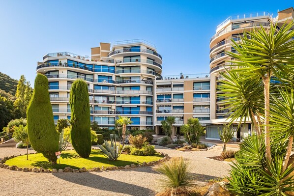 A multi-story hotel with balconies, a landscaped garden, and a clear sky.