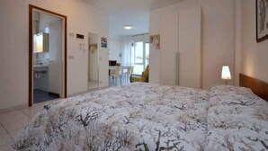 Ein Schlafzimmer mit einem großen Bett, einem Schreibtisch und einem Stuhl, sowie ein Badezimmer und Blick ins Freie.