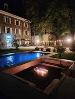 A swimming pool with a fire feature, surrounded by outdoor seating and a building with multiple windows.