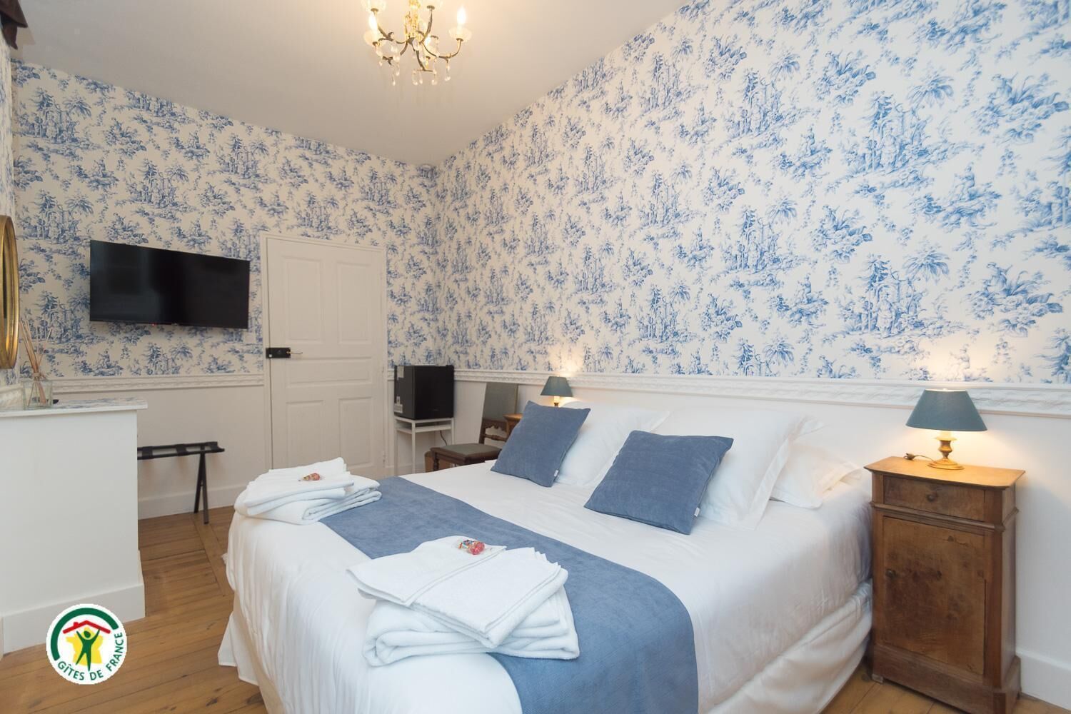 A hotel room with a bed, bedside lamps, a TV, and a desk with a chair.