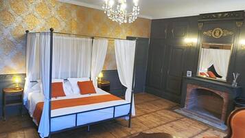 A four-poster bed with a canopy, a fireplace, a mirror, and a seating area with a chair and table.