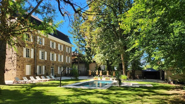 A courtyard with a swimming pool, lounge chairs, and a building with a stone facade. - Château de la Rochetière (Marcilloles)