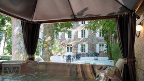 A hot tub with a view of a stone building and trees. - Château de la Rochetière (Marcilloles)
