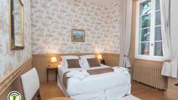 A hotel room with a bed, a nightstand, a chair, a window with curtains, and a radiator.