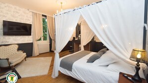 A bedroom with a four-poster bed, a television, a chair, and a nightstand with a lamp. - Château de la Rochetière (Marcilloles)