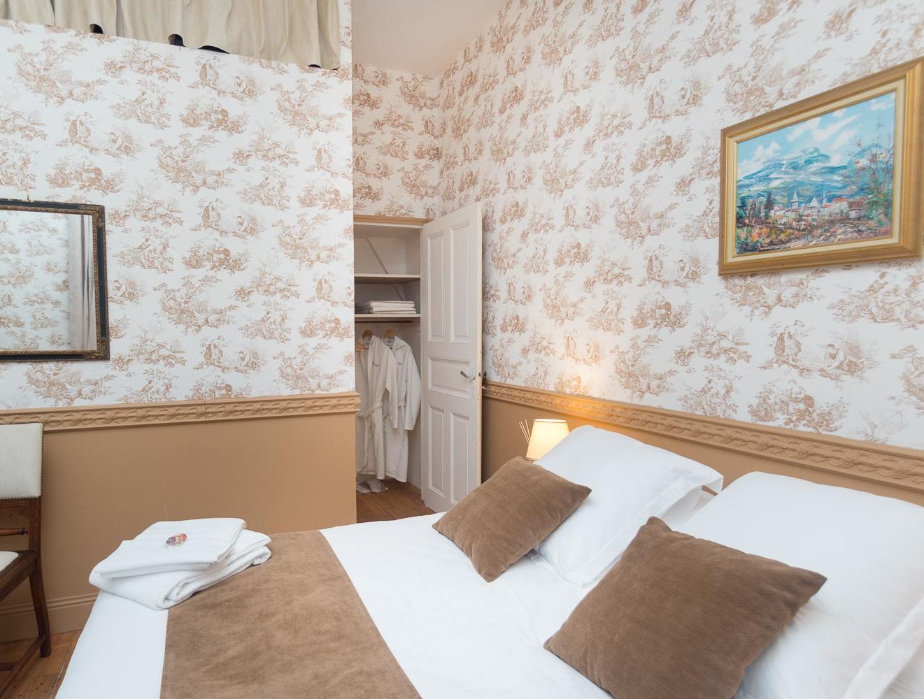 Una camera d'albergo con un letto, una sedia, un armadio e un quadro appeso al muro.