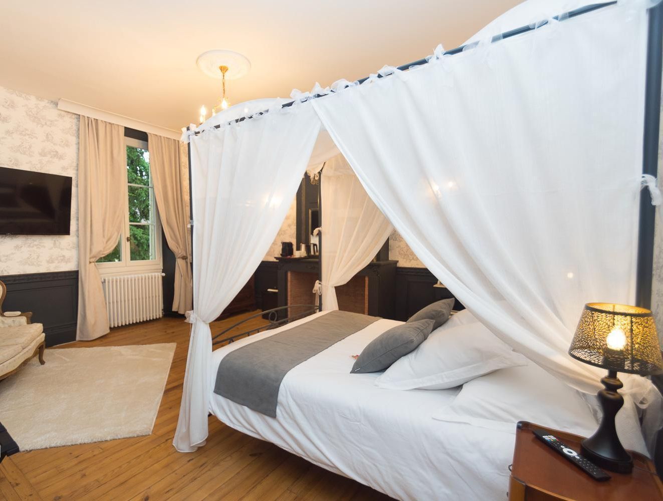 Ein Schlafzimmer mit einem Himmelbett, einem Fernseher, einem Sessel und einem Nachttisch mit einer Lampe.