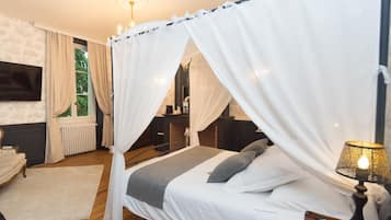 Ein Schlafzimmer mit einem Himmelbett, einem Fernseher, einem Sessel und einem Nachttisch mit einer Lampe.