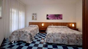 Habitación de hotel con dos camas, suelo de cuadros, cabecero de madera, un reloj de pared y un cuadro con flores.