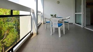 Un balcón con mesa y sillas, una puerta corrediza de vidrio y vistas a zonas verdes.