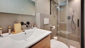 Un baño moderno con un lavamanos grande, cabina de ducha de vidrio y artículos de tocador sobre la encimera.