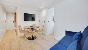 Una sala moderna con una mesa redonda para comer, sillas de mimbre, un sofá azul y un televisor de pantalla plana montado en la pared.