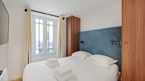 Habitación de hotel con una cama, un armario de madera, una pared decorada en azul y una ventana con cortinas.
