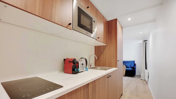 Una cocina moderna con armarios de madera, microondas integrado, hervidor y un lavabo.