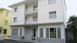 Ein zweistöckiges Gebäude mit einem Balkon im zweiten Stock, einem verschlossenen Eingangsbereich und einer kleinen Veranda.