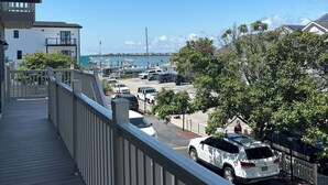 A balcony with a view of a marina, parked cars, and a clear blue sky. - White Marlin & Concerts | 2BR w/ Pool & Parking (Ocean City)