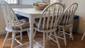 A dining area with a white table and chairs, a basket with items, and a window with blinds. - White Marlin & Concerts | 2BR w/ Pool & Parking (Ocean City)
