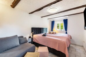 A bedroom with a bed, a grey sofa, a bedside table, and a window with curtains. - Apartment Schlossmühle in Bigge-Olsberg (Olsberg)